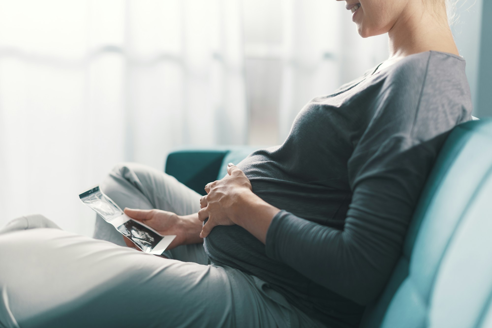 Pregnant woman sitting on the sofa and watching ultrasound images of her baby