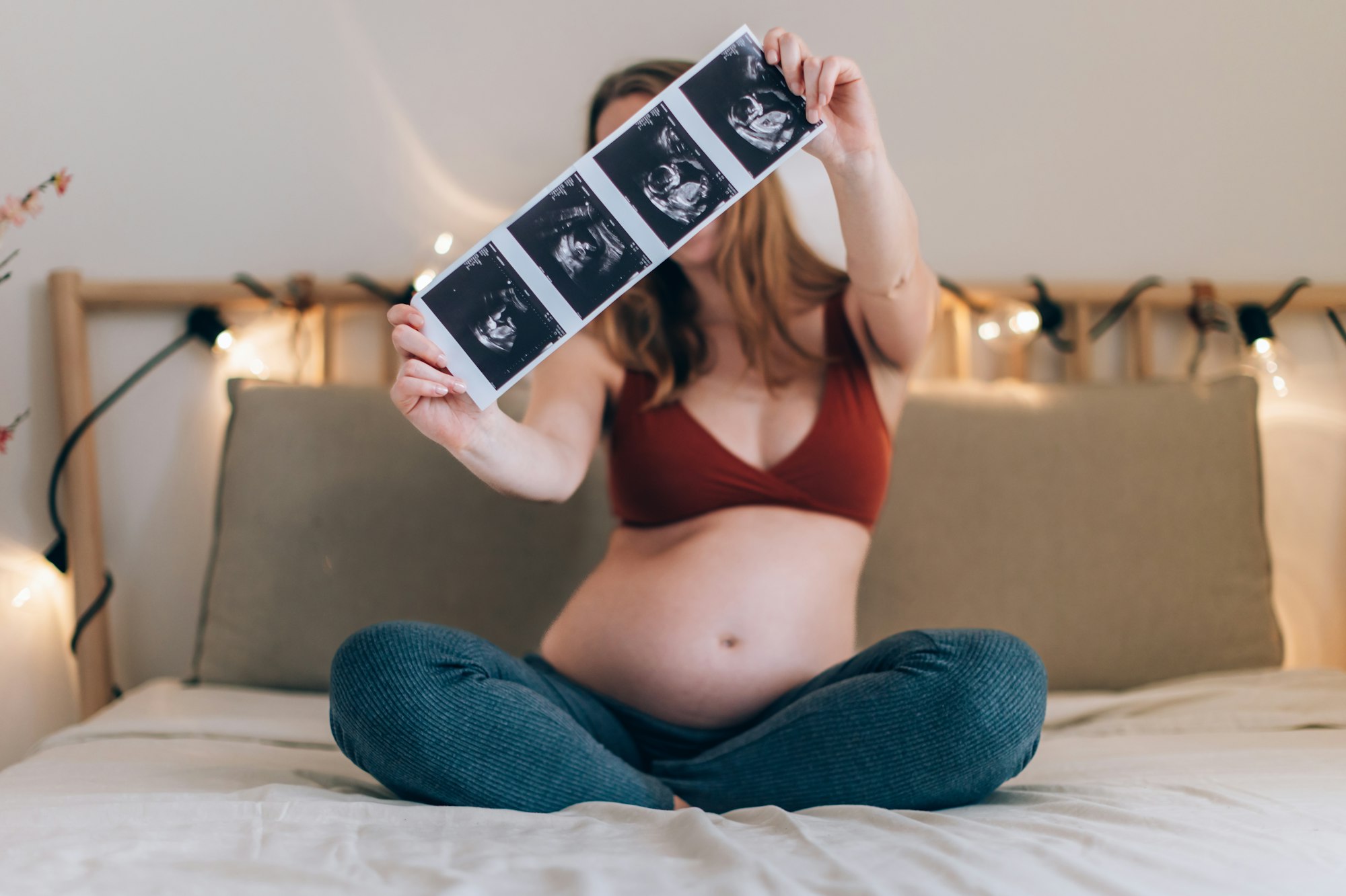 white, blonde pregnant woman sitting cross-legged on the bed